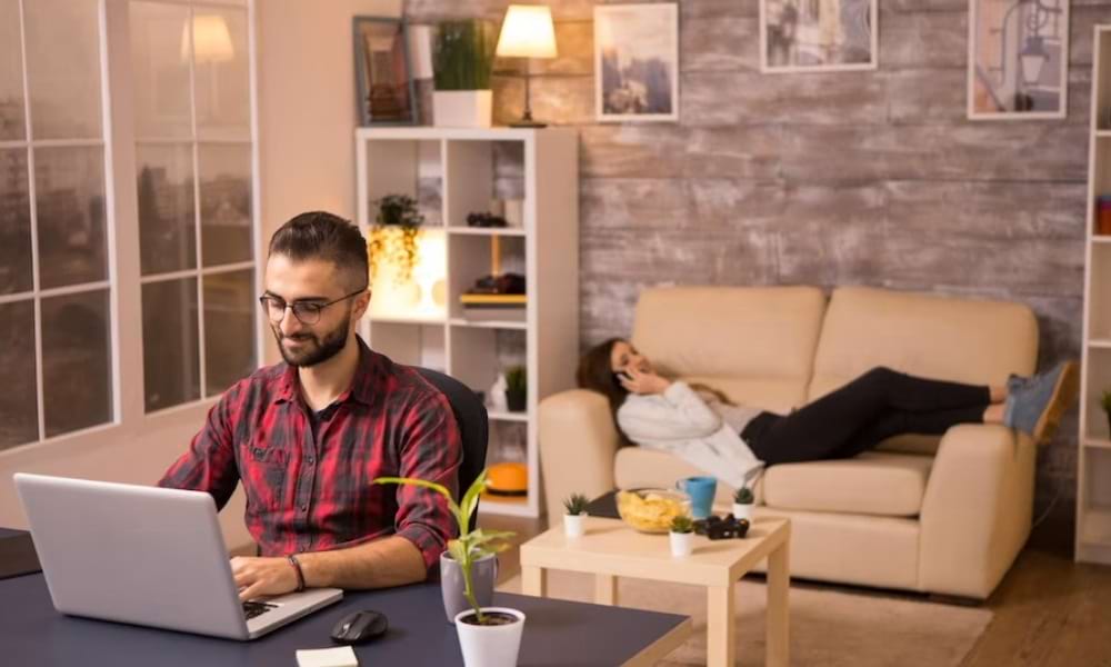 Home office pár nő kanapén telefonál férfi asztalnál dolgozik számítógép előtt